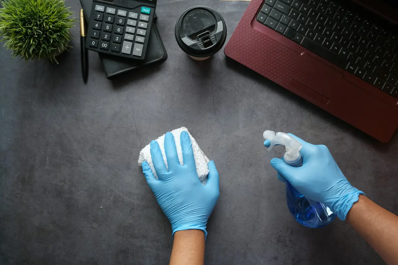 Mains gantées nettoyant un bureau avec un vaporisateur et un chiffon