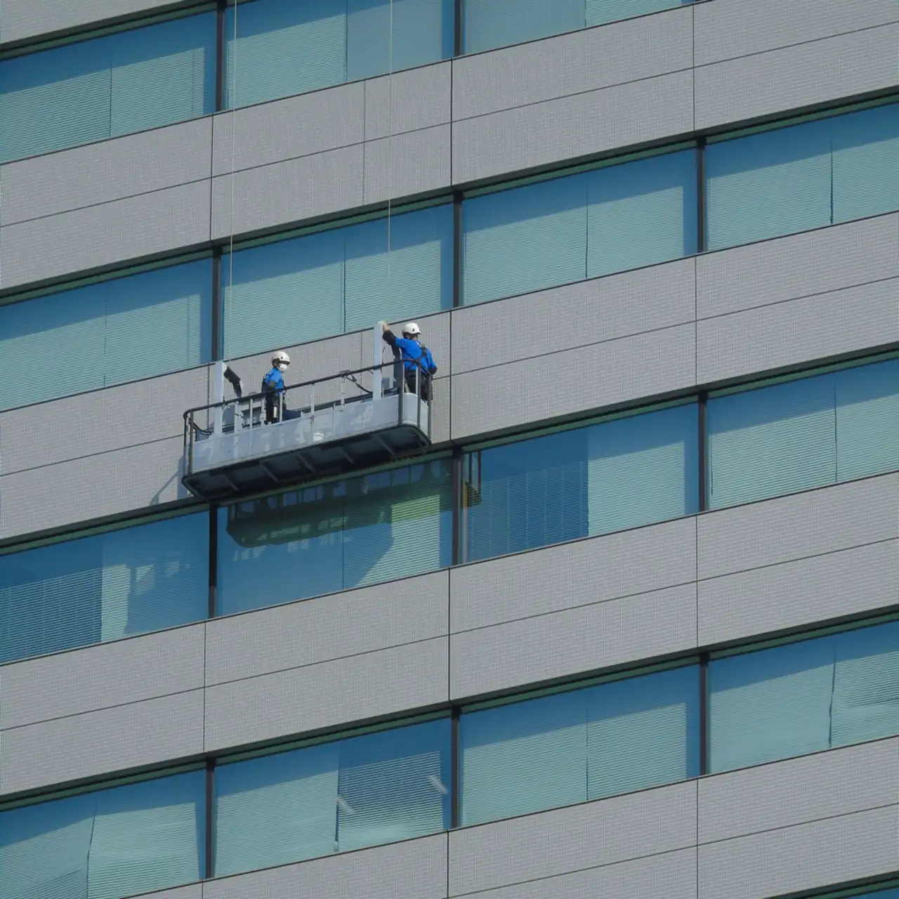 Deux laveurs de vitres en nacelle nettoyant une façade vitrée