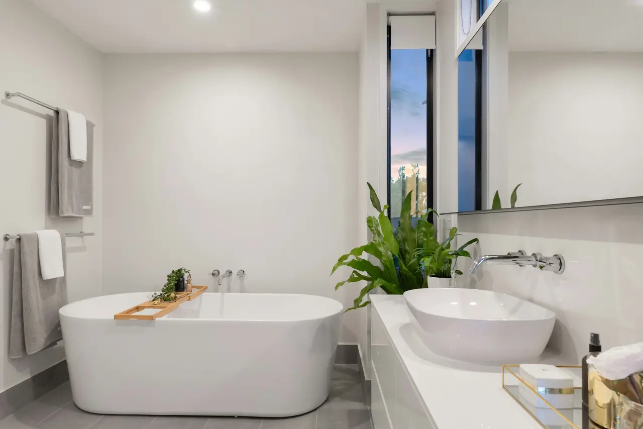 Salle de bain blanche impeccable, baignoire îlot, vasque et plante verte